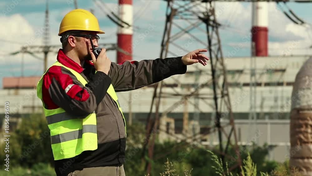 Factory worker with portable radio transmitter on electric power station. Power engineering specialist on heat power plant communicates via radio station Factory worker with portable radio transmitter on electric power station. Power engineering specialist on heat power plant communicates via radio station