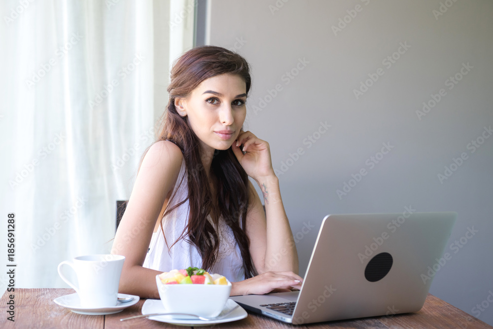 Woman having coffee and working outside. Working on laptop during her vacation in a tropical hotel. White female with white dress. Agile. modile office concept.