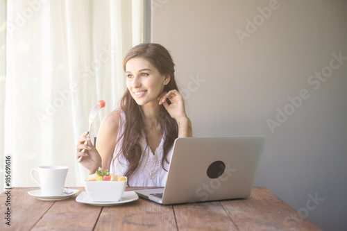Woman having coffee and working outside. Working on laptop during her vacation in a tropical hotel. White female with white dress. Agile. modile office concept.