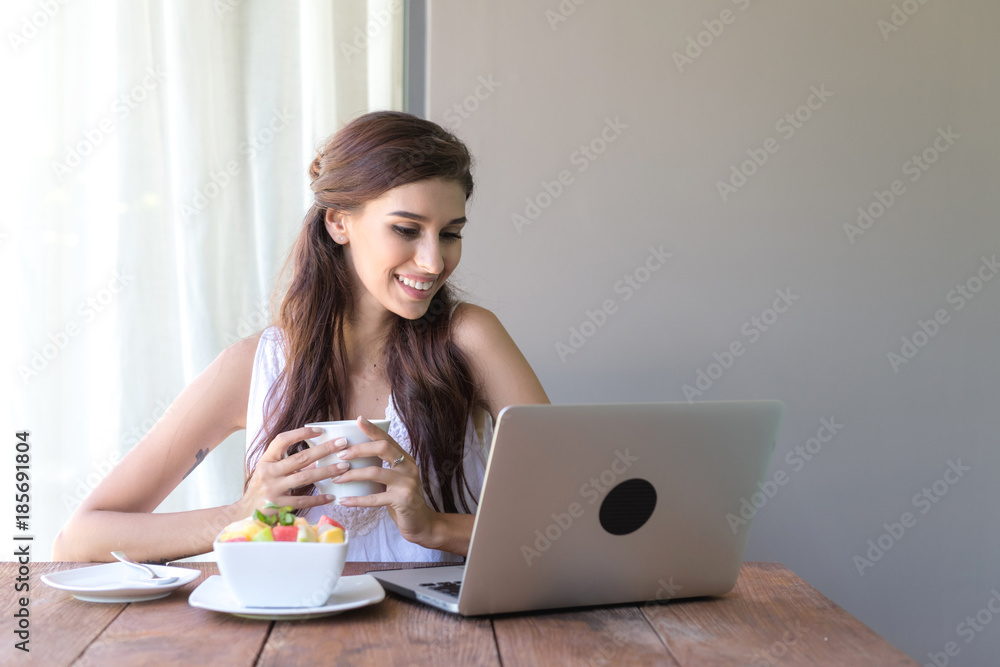 Woman having coffee and working outside. Working on laptop during her vacation in a tropical hotel. White female with white dress. Agile. modile office concept. Woman having coffee and working outside. Working on laptop during her vacation in a tropical hotel. White female with white dress. Agile. modile office concept.