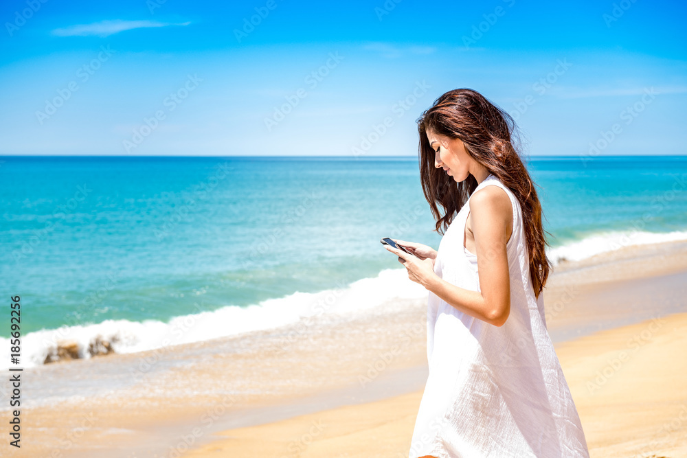 Beautiful young single white woman on beach. Using mobile phone calling her friends, wearing white dress. Connected world concept. Beautiful young single white woman on beach. Using mobile phone calling her friends, wearing white dress. Connected world concept.