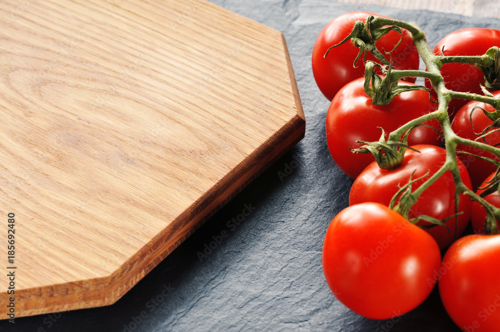 Fresh tomatoes on a branch with the cutting board on a dark background Fresh tomatoes on a branch with the cutting board on a dark background