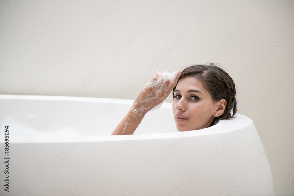 Beautiful young white woman enjoy relaxing in bubble bath. Resting, relaxing, touhing her arm, smiling. White caucasian woman. Beautiful young white woman enjoy relaxing in bubble bath. Resting, relaxing, touhing her arm, smiling. White caucasian woman.
