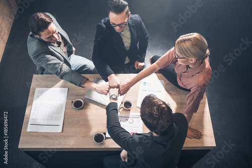 Top view cheerful female and male colleagues holding arms together while sitting at table in office. Profession and relation concept photo