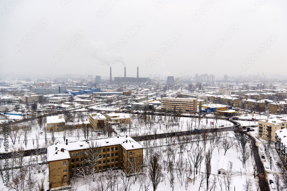 The aerial View of urban fringes in Kyiv,Ukraine in foggy winter day.View over the city rooftops with snow at Kiev suburb.Heating Power Plant,moderns buildings,uptown/Winter Industrial cityscape