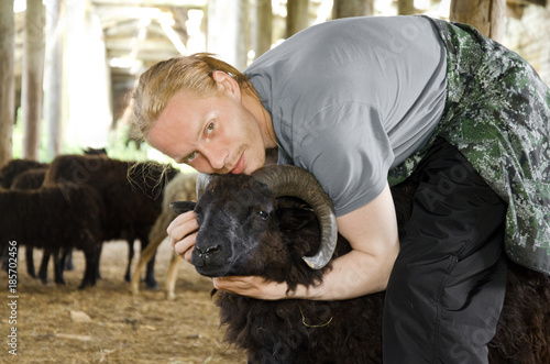 man hugs the black sheep on the farm