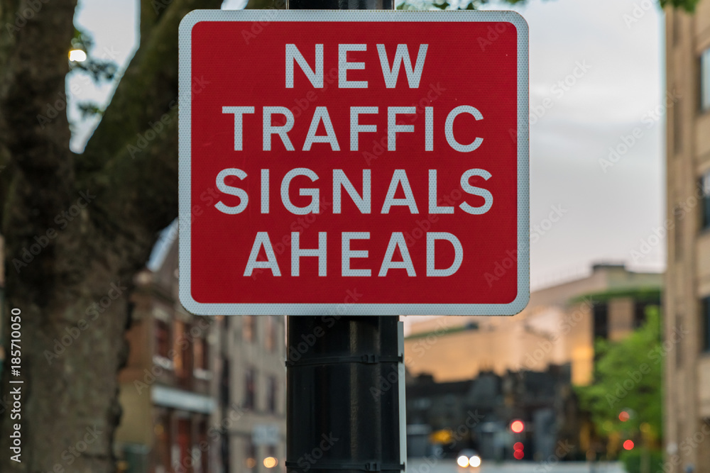 Sign: New traffic signals ahead, with some blurry traffic signals in the background, seen in Ipswich, Suffolk, England, UK Sign: New traffic signals ahead, with some blurry traffic signals in the background, seen in Ipswich, Suffolk, England, UK