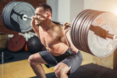 Muscular man training squats with barbells on shoulders.