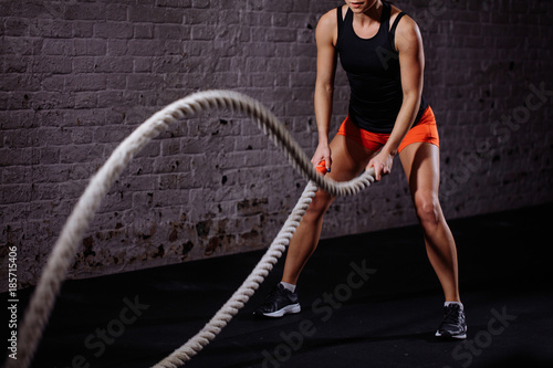 Woman training with battle rope in cross fit gym