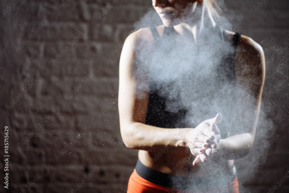 Cropped shot of young female athlete clapping hands with chalk powder before strength training