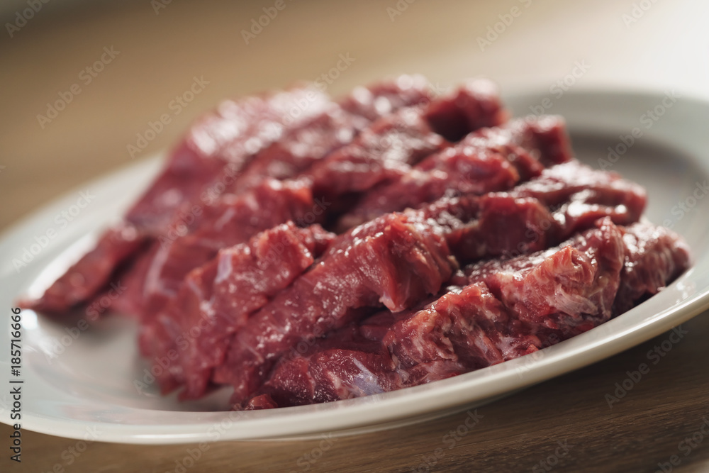slices of raw beef in white plate on kitchen table