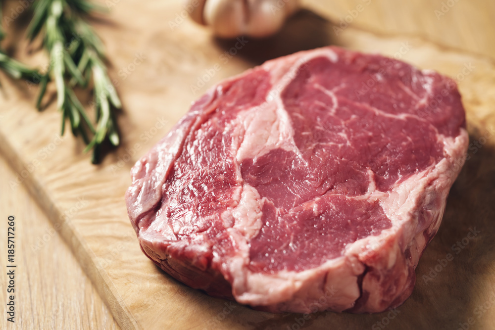 fresh raw rib eye steak on wood board on kitchen table