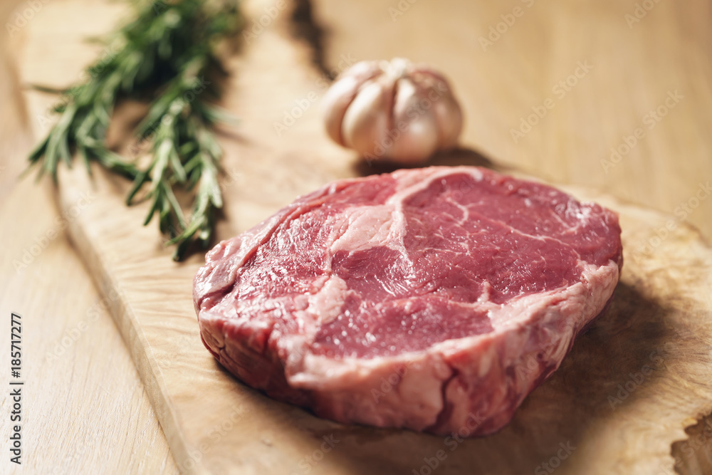 fresh raw rib eye steak on wood board on kitchen table