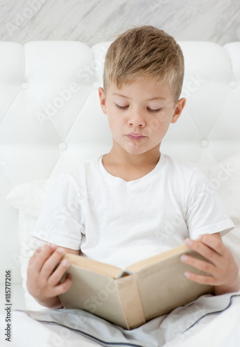 boy is reading a book on the bed