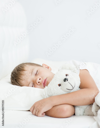 the boy is sleeping on the bed hugging a toy bear
