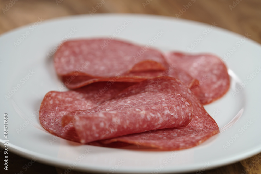 sliced salami on white plate on wood table