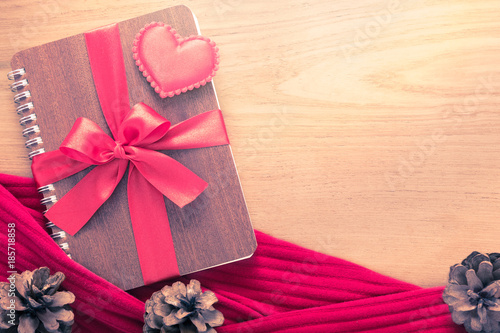 Valentine or love theme, felt heart sitting on notebook wrapped in red ribbon on wooden table photo