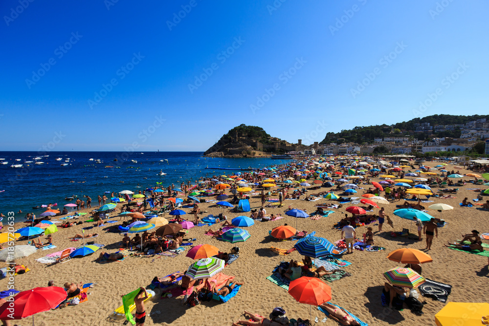 View of the beach full of people in the month of August, with the castle in the background, in Tossa de Mar, Girona, Spain