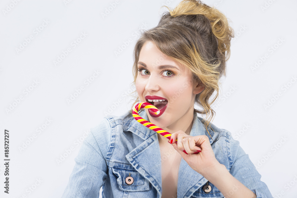 Food Ideas and Concepts. Portrait of Young Surprised Caucasian Blond Girl Eating Big Red-Yellow Candy Cane. Against White Background Food Ideas and Concepts. Portrait of Young Surprised Caucasian Blond Girl Eating Big Red-Yellow Candy Cane. Against White Background