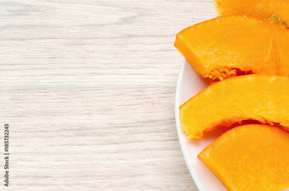 Pumpkin pieces on a white plate, on a wooden base, ready for cooking Pumpkin pieces on a white plate, on a wooden base, ready for cooking
