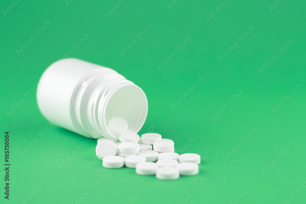 Close up white pill bottle with spilled out pills on jade green background with copy space. Focus on foreground, soft bokeh. Pharmacy drugstore concept Close up white pill bottle with spilled out pills on jade green background with copy space. Focus on foreground, soft bokeh. Pharmacy drugstore concept