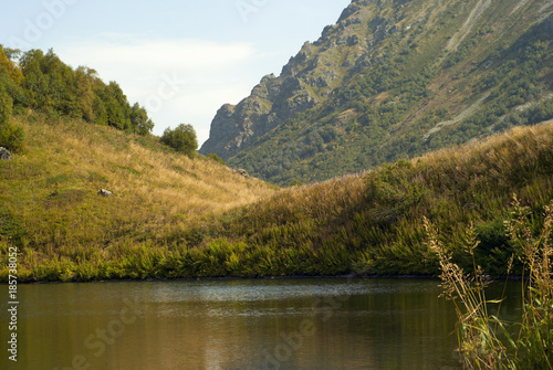 shore of a small mountain lake against a background of a blurred rocky mountain range on a sunny autumn day