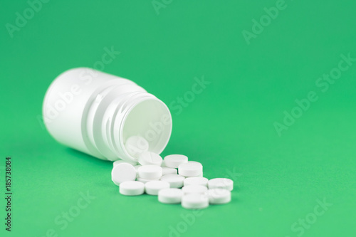 Close up white pill bottle with spilled out pills on jade green background with copy space. Focus on foreground, soft bokeh. Pharmacy drugstore concept