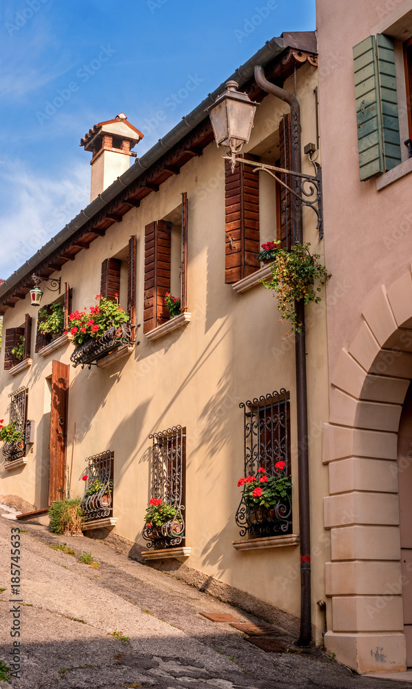 Cozy little street in Conegliano. Windows with blinds are decorated with flowers.