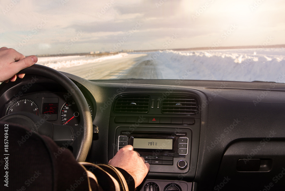 man driving a car, driving in winter on snow-covered road in front of the sunset. listening to music adding to the maximum sound. vehicle management, interior.