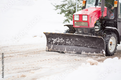 Red tractor cleaning the streets of large amounts of snow in city after snowfall. Winter time concept.