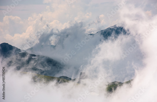 cloud formation in mountains on high altitude. spectacular natural phenomenon in summer. lovely weather background of hills with snow and grass © Pellinni