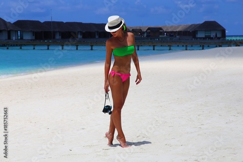 tanned girl in bikini and photo camera on white sand in tropical island photo