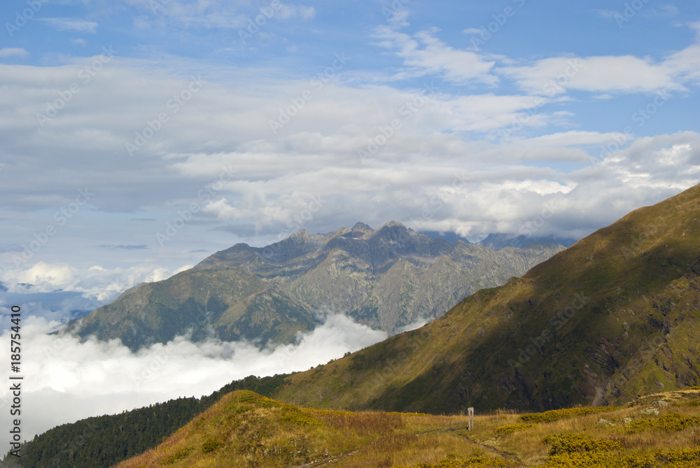 morning view from a mountain plateau to neighboring mountain ranges, towering above the clouds; near is the trail of the tourist route with a road sign.. morning view from a mountain plateau to neighboring mountain ranges, towering above the clouds; near is the trail of the tourist route with a road sign..