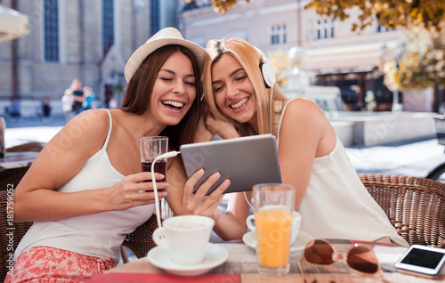 Friends meeting in a cafe. Young women drinking coffee and have fun with tablet. Consumerism  lifestyle concept