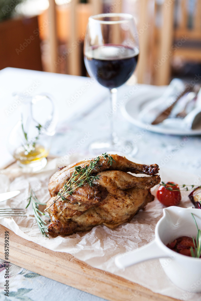 Baked quail with salad and cherry tomatoes on a wooden board with a glass of wine