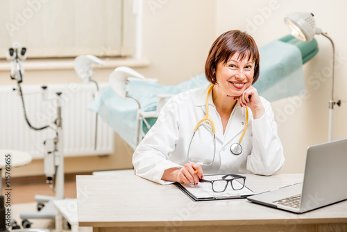 Portrait of a smiling seinor doctor sitting with laptop and documents in the gynecological office photo