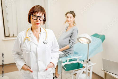Portrait of a senior woman gynecologist standing in the office with patient on the background