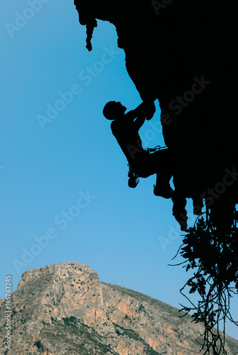 Silhouette of a rock climber on an overhanging rock against the backdrop of a rocky island