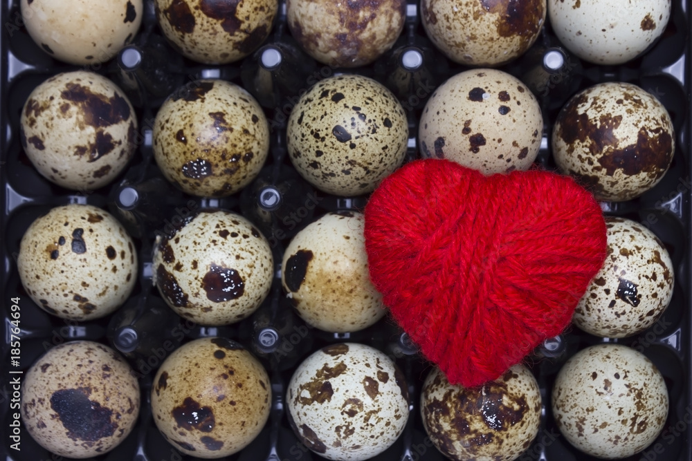 Fototapeta premium An overhead photo of fresh small uncooked quail eggs in the black plastic container and red heart. I like Healthy lifestyle, healthy eating food concept.
