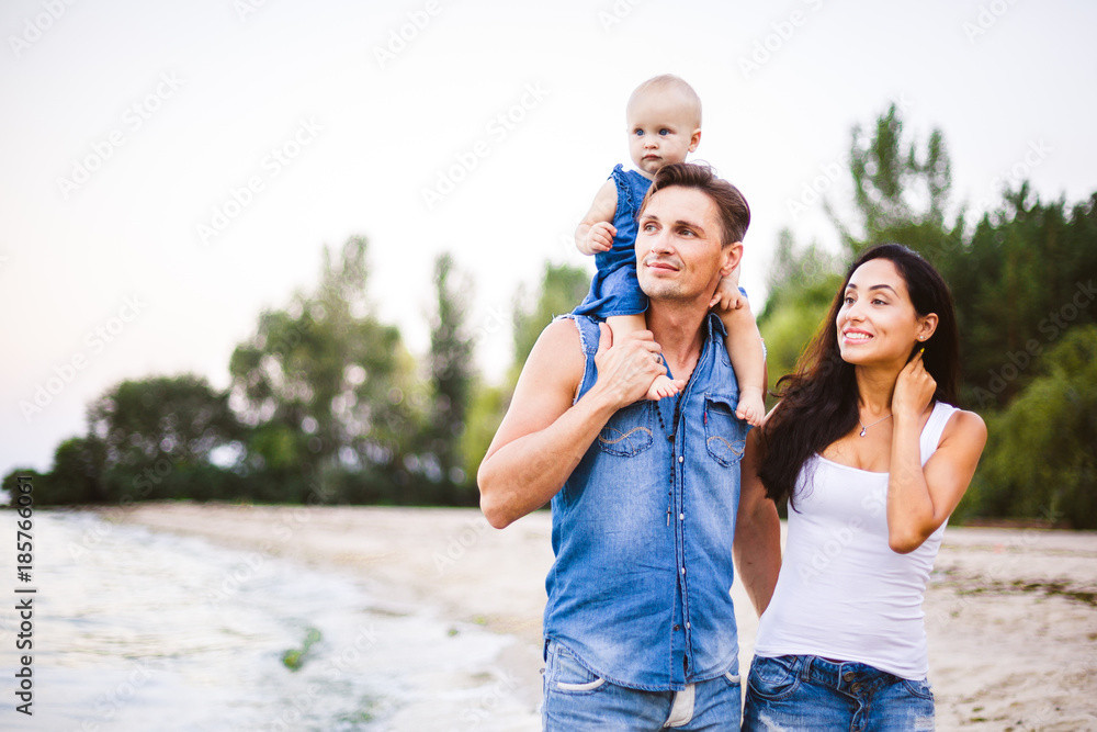 beautiful young family on vacation with baby. The father holds the blonde girl in her arms, and the brunette's mother hugs her husband. The concept of a family beach holiday summer near the sea beautiful young family on vacation with baby. The father holds the blonde girl in her arms, and the brunette's mother hugs her husband. The concept of a family beach holiday summer near the sea