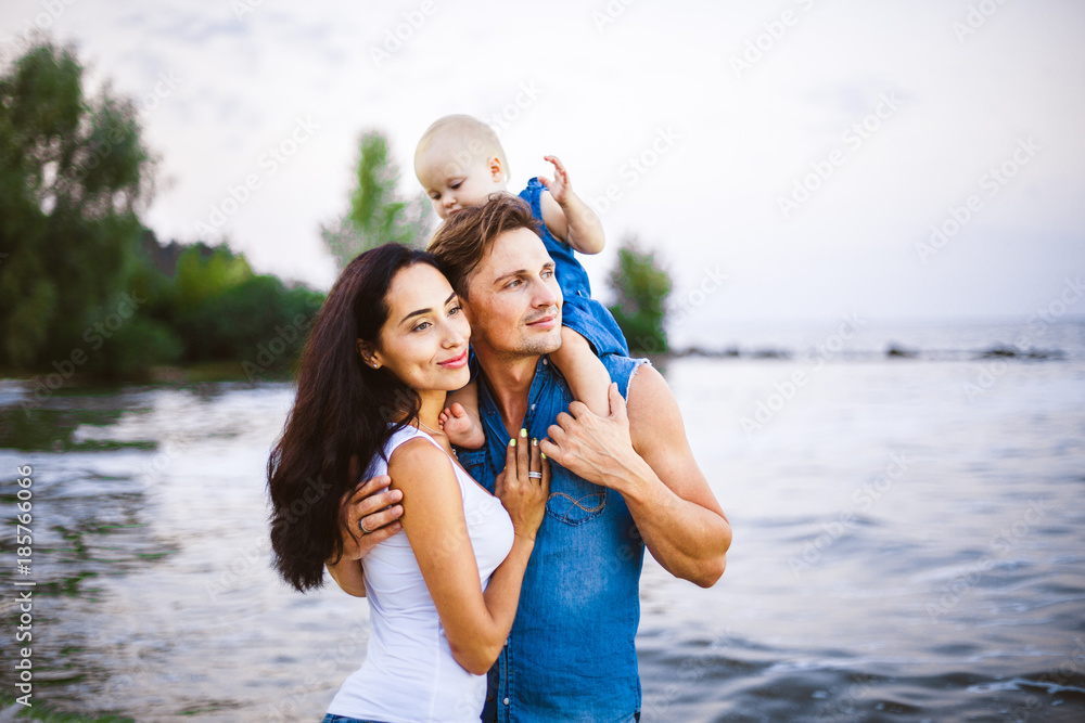 beautiful young family on vacation with baby. The father holds the blonde girl in her arms, and the brunette's mother hugs her husband. The concept of a family beach holiday summer near the sea beautiful young family on vacation with baby. The father holds the blonde girl in her arms, and the brunette's mother hugs her husband. The concept of a family beach holiday summer near the sea