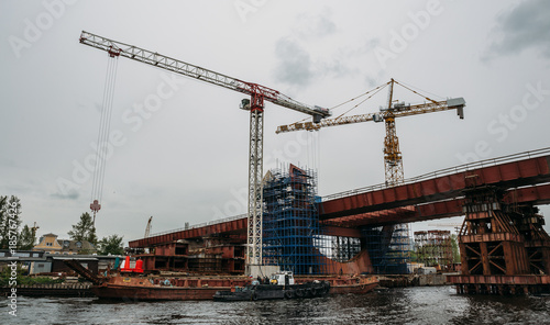 Construction of bridge with cranes and equipment over river in industrial zone in St. Petersburg