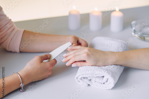 Close up of beautiful female hands having spa manicure at beauty salon. Woman hands care. Polishing nails by using nail files. Nail treatment.