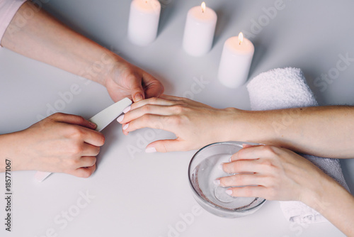 Close up of beautiful female hands having spa manicure at beauty salon. Woman hands care. Polishing nails by using nail files. Nail treatment. Top view.