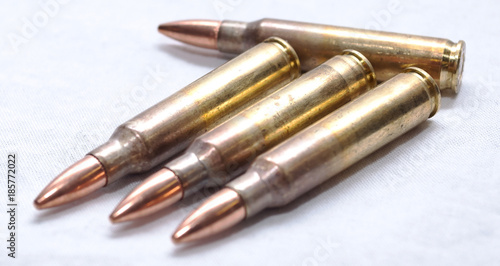 Four .223 caliber rifle bullets, three lined up together on an angle with the other one above them on a white background