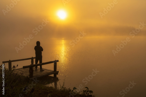 Silhouette Depressed man standing on the houseboat river lake at the sunrise time, dramatic and loneliness concept