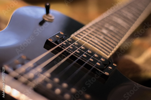 Fragment of the black electric guitar deck, pickup, neck and strings. Warm tones photo