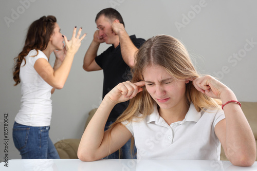 girl teenager closes ears in the background screaming at each other parents.