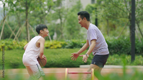 Asian father & son playing basketball in garden in morning