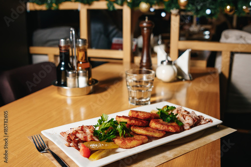 Potato pancakes with bacon on a white rectangular plate on a table in a restaurant. Table setting at the restaurant.